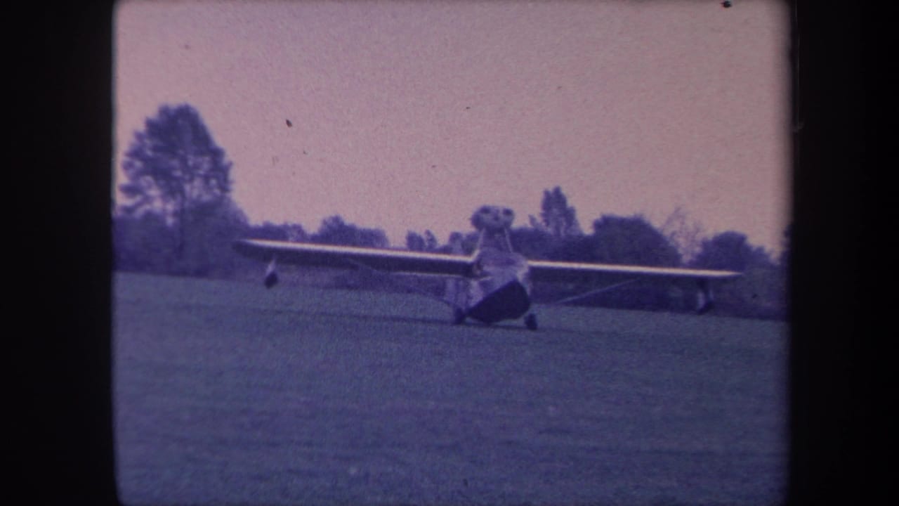 High-wing single-engine aircraft on a grass airfield, California circa 1959, 8mm home movie with pronounced blue-magenta dye fade and film grain.