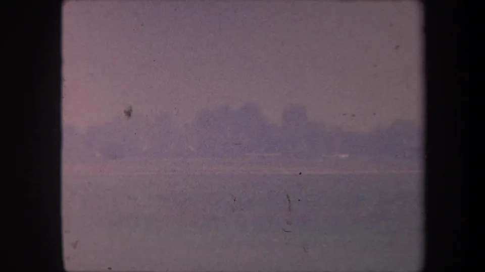 Overexposed 8mm frame from circa 1959 California airfield sequence; faint horizon tree line under pale washed-out sky with visible film scratches.