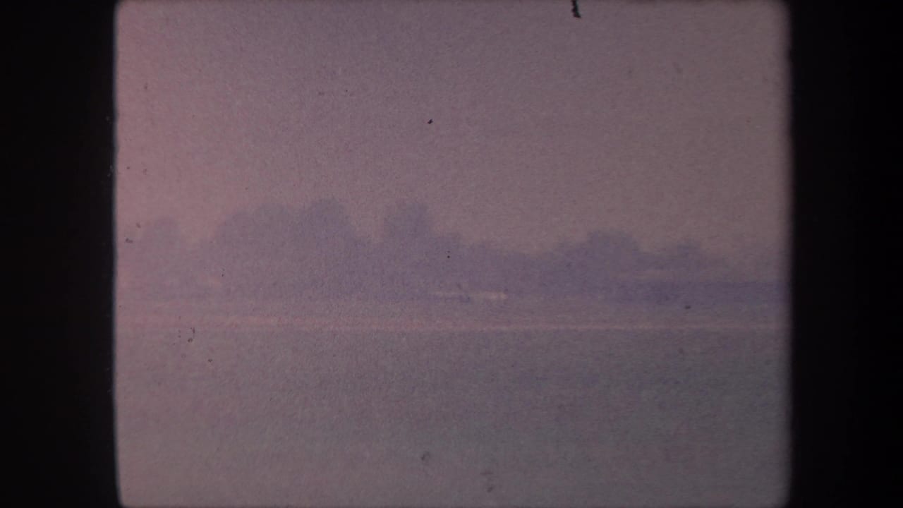 1959 8mm home movie frame: soft pink-shifted sky over a flat horizon, possibly a California airfield or waterway; no figures visible.