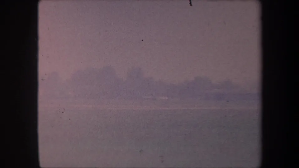 1959 8mm home movie frame: soft pink-shifted sky over a flat horizon, possibly a California airfield or waterway; no figures visible.