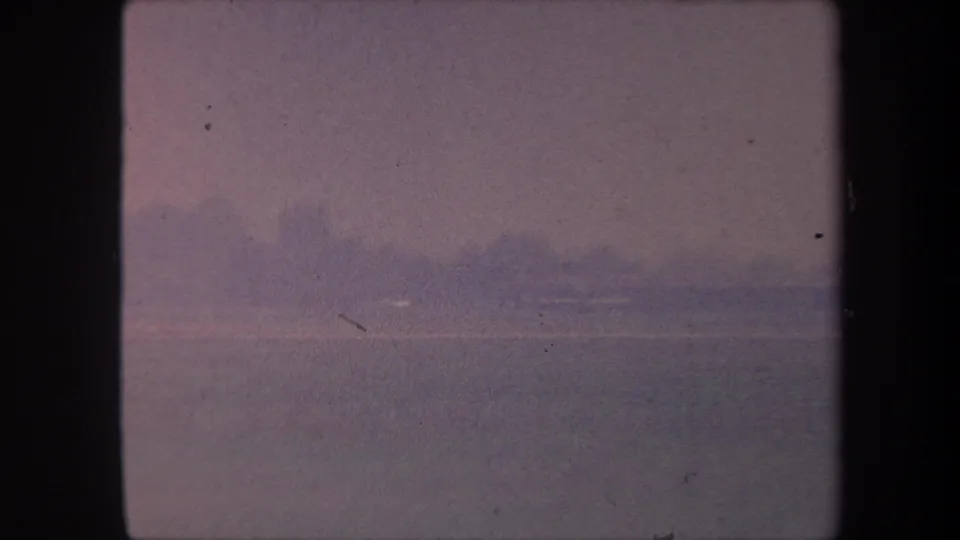 1959 8mm home movie frame: open pink sky and flat horizon with a faint white element near the horizon line and a visible horizontal scratch mark.