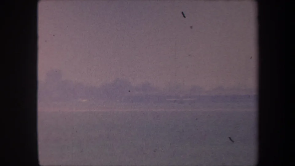 1959 8mm home movie frame: pink-lavender sky over a low distant land silhouette, consistent composition throughout the clip, with scattered dust spots.