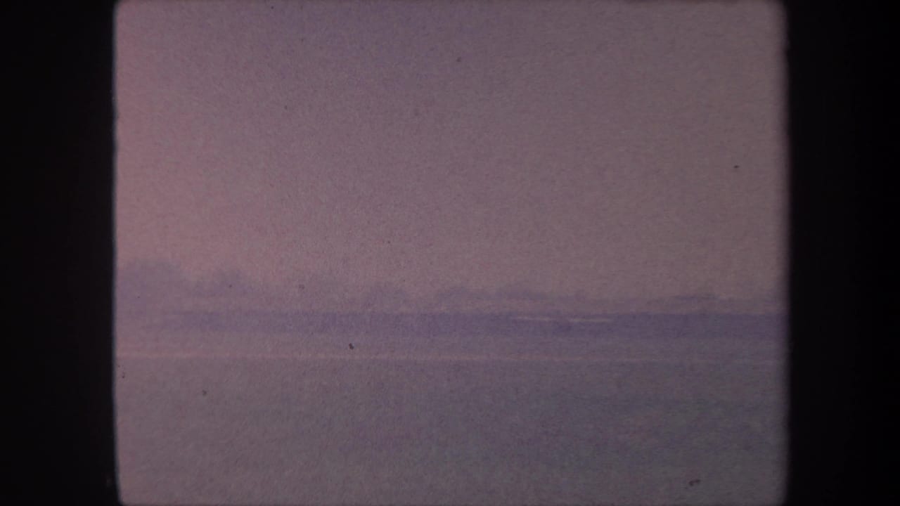 8mm home movie frame circa 1959, California: washed-out purple-pink sky over flat landscape, very low contrast with no identifiable subjects.