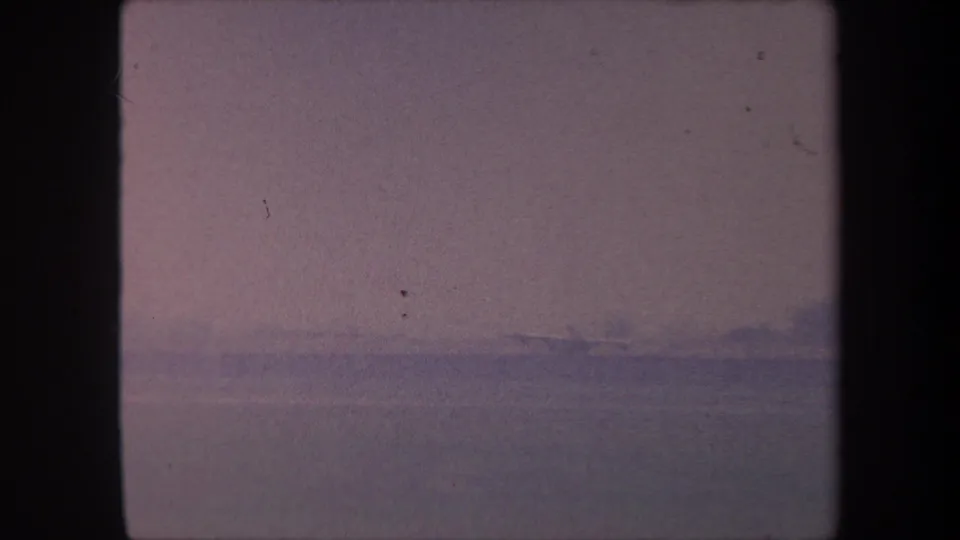 8mm home movie frame circa 1959, California: purple-toned hazy sky over flat landscape with visible film scratches and dust artifacts.