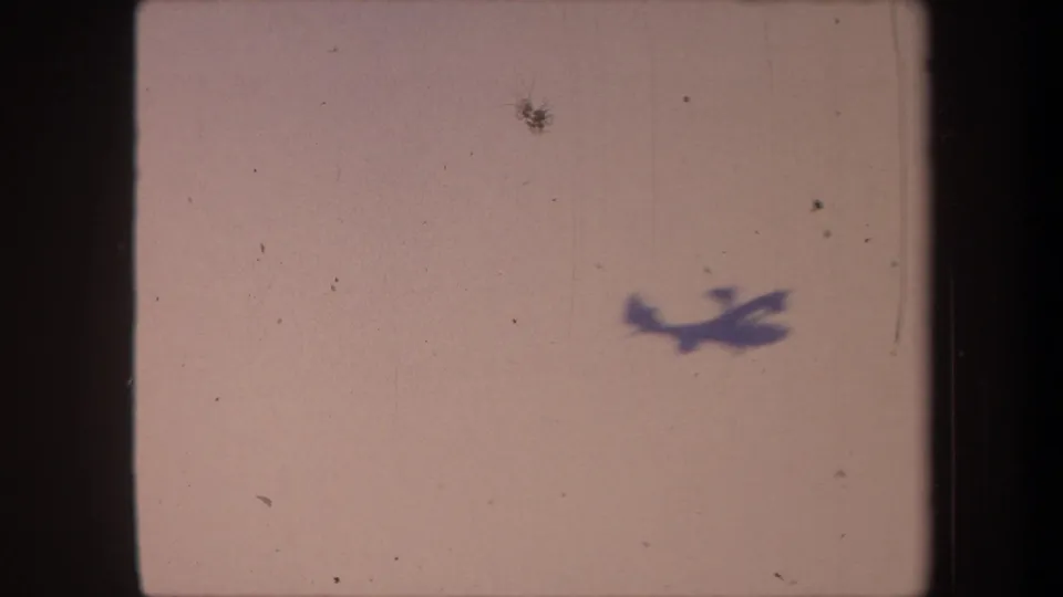 Propeller aircraft in lower-center of frame showing slight motion blur against pale pinkish sky; 8mm home-movie, Yucaipa, California, 1959.