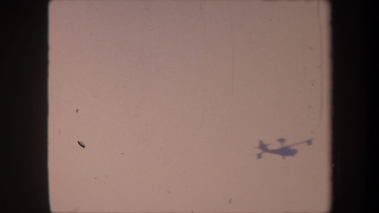 Small aircraft silhouette traversing a faded pale-pink 8mm sky, likely filmed in Yucaipa, California, circa 1959.