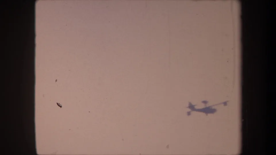 Small aircraft silhouette traversing a faded pale-pink 8mm sky, likely filmed in Yucaipa, California, circa 1959.