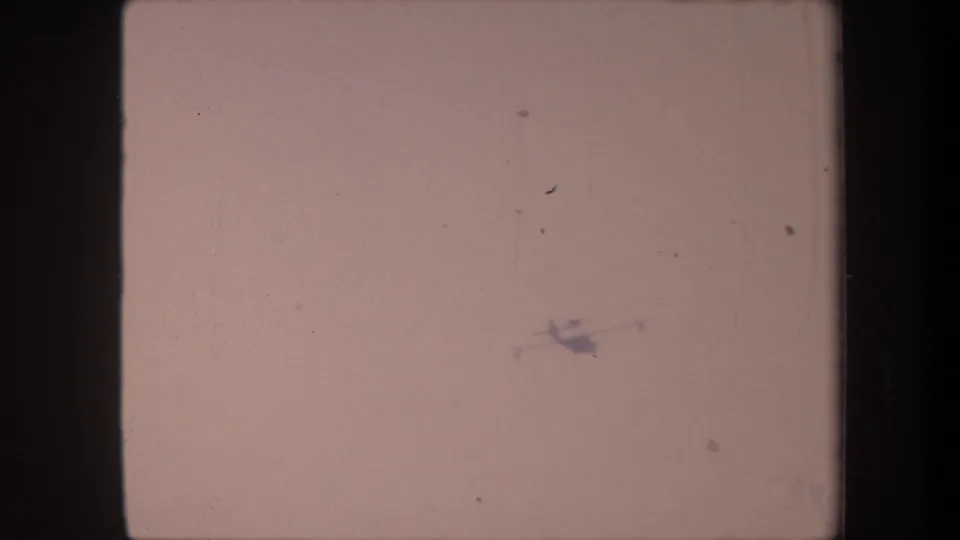 Aircraft silhouette in the lower center of the 8mm frame, dust spots prominent, from a circa 1959 California home movie.