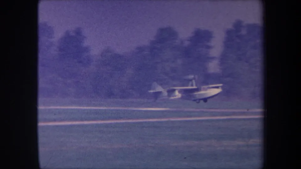 Seaplane accelerating or decelerating on a grass strip, likely Yucaipa, California, circa 1959; motion blur and 8mm grain evident.