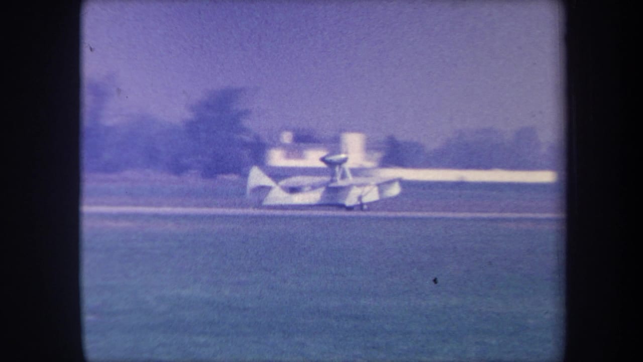 Small white amphibious aircraft taxiing across a grass airfield, circa 1959; the bystander from the opening frame has moved out of view.
