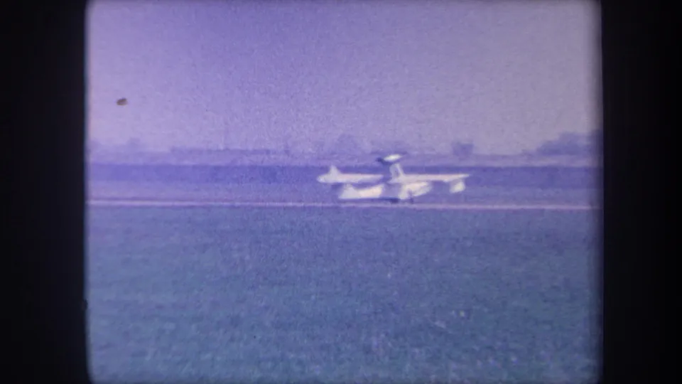Small amphibious aircraft near the far edge of a grass airfield, circa 1959; aircraft is smaller in frame as it continues to move away.