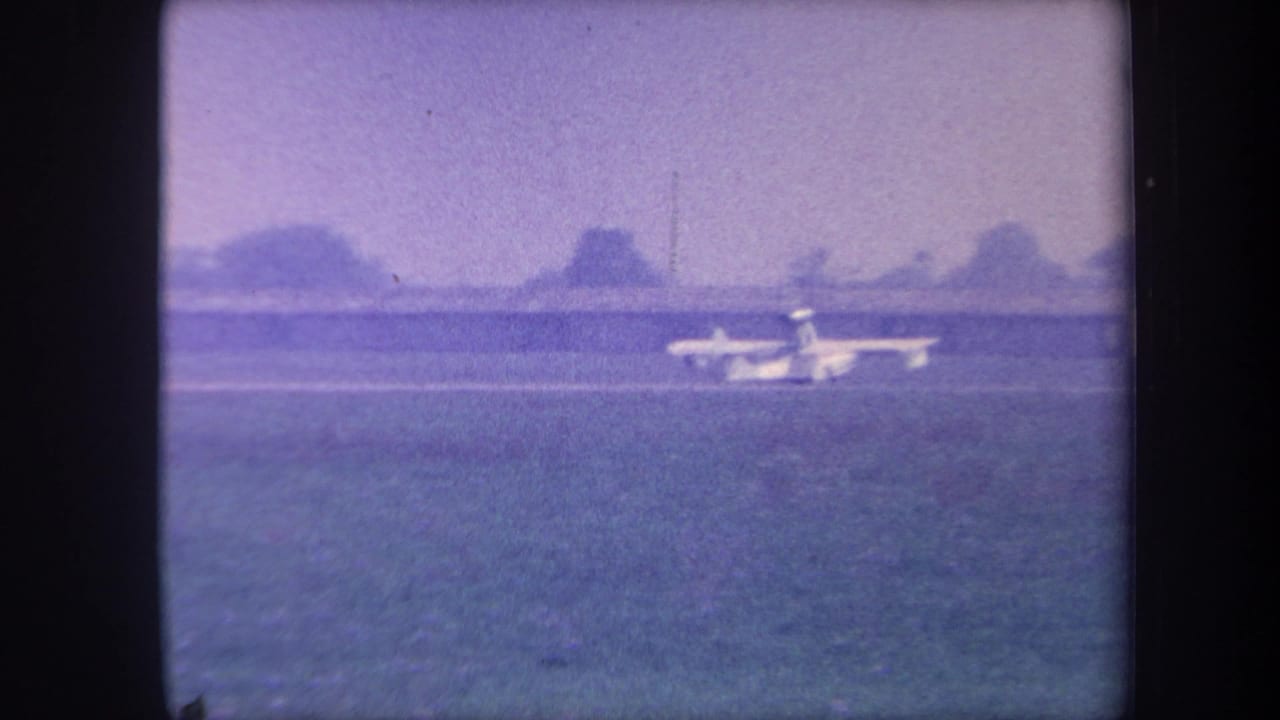 Small aircraft accelerating down a rural grass runway with tree line and open sky, 8mm home movie circa 1959, possibly Yucaipa, California.