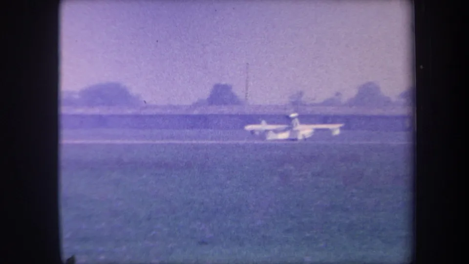 Small aircraft accelerating down a rural grass runway with tree line and open sky, 8mm home movie circa 1959, possibly Yucaipa, California.