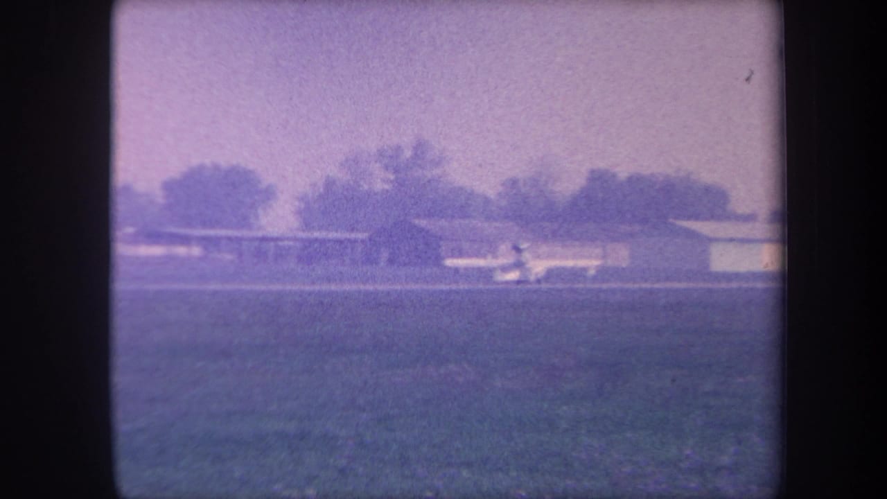 Small single-engine aircraft on a rural airstrip near a flat-roofed hangar, Southern California, circa 1959, 8mm home movie with characteristic purple-violet color shift.