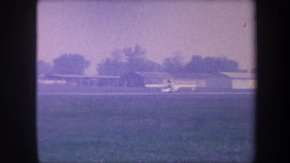 Small single-engine aircraft on a rural airstrip near a flat-roofed hangar, Southern California, circa 1959, 8mm home movie with characteristic purple-violet color shift.