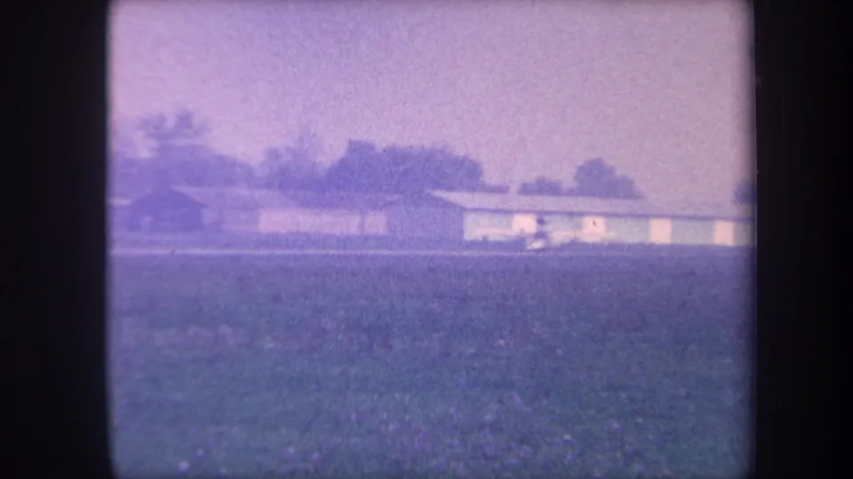 8mm home movie from approximately 1959 showing a small rural airfield near Yucaipa, California, with a low panel-clad hangar and trees under a purple-tinted sky.