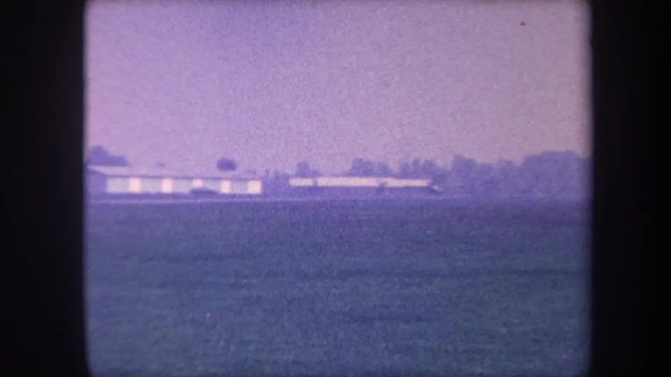 Pulled-back 8mm frame from circa 1959 showing the full expanse of a rural Southern California airfield with hangar sitting low on the horizon.