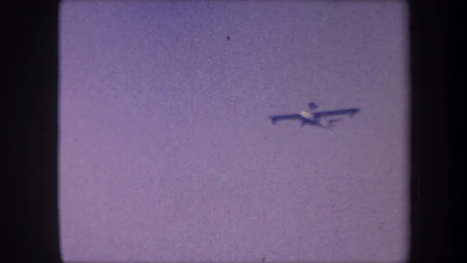 Light propeller aircraft mid-flight, 1959 8mm home movie, sky-fill frame with purple dye shift and no horizon visible.