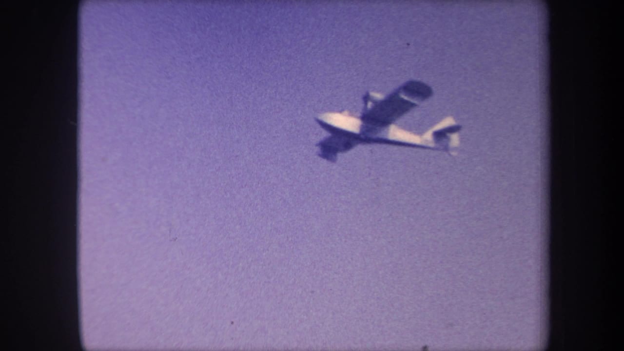 Small single-engine aircraft in flight, upper-left of frame, against a purple-tinted 8mm sky.