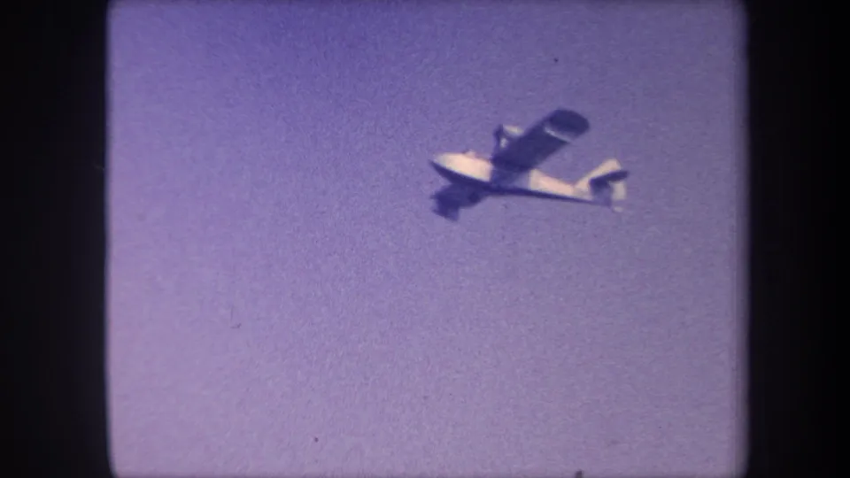 Small single-engine light aircraft tracked in flight against a purple-cast sky, from 8mm home movie footage, Yucaipa, California, circa 1959.