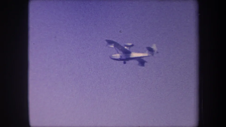 Single-engine light aircraft in level flight, silhouetted against purple-cast sky, 8mm home movie, California, circa 1959.