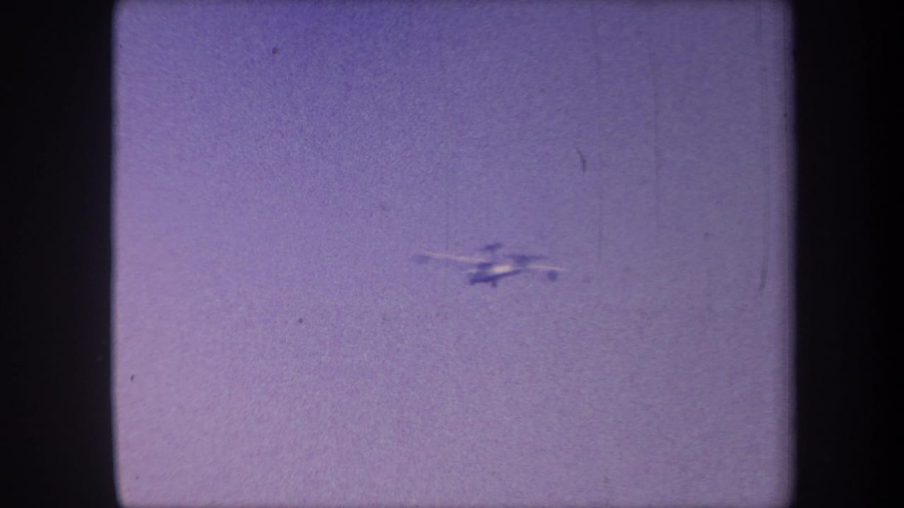 Small aircraft visible upper-right, smaller and more distant against a lavender sky on 8mm film.