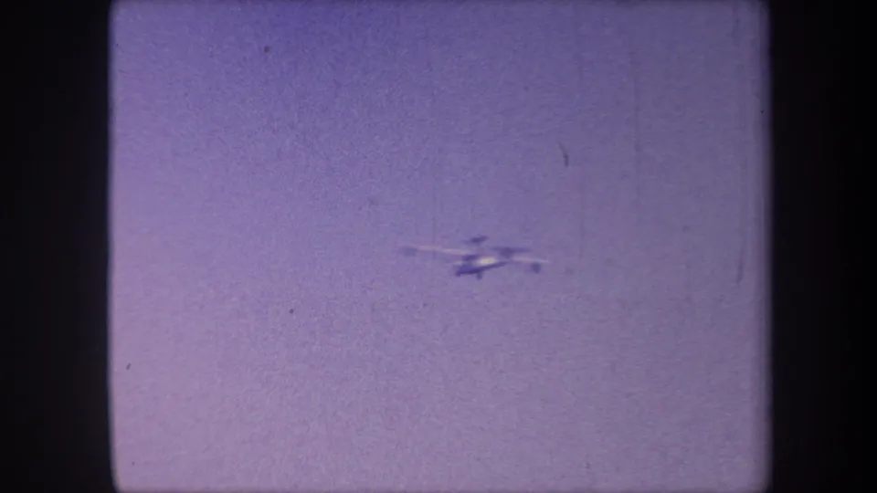 The propeller aircraft, now further away in the upper-right of frame, continues its tracked path across a lavender sky in this 1959 California home movie.
