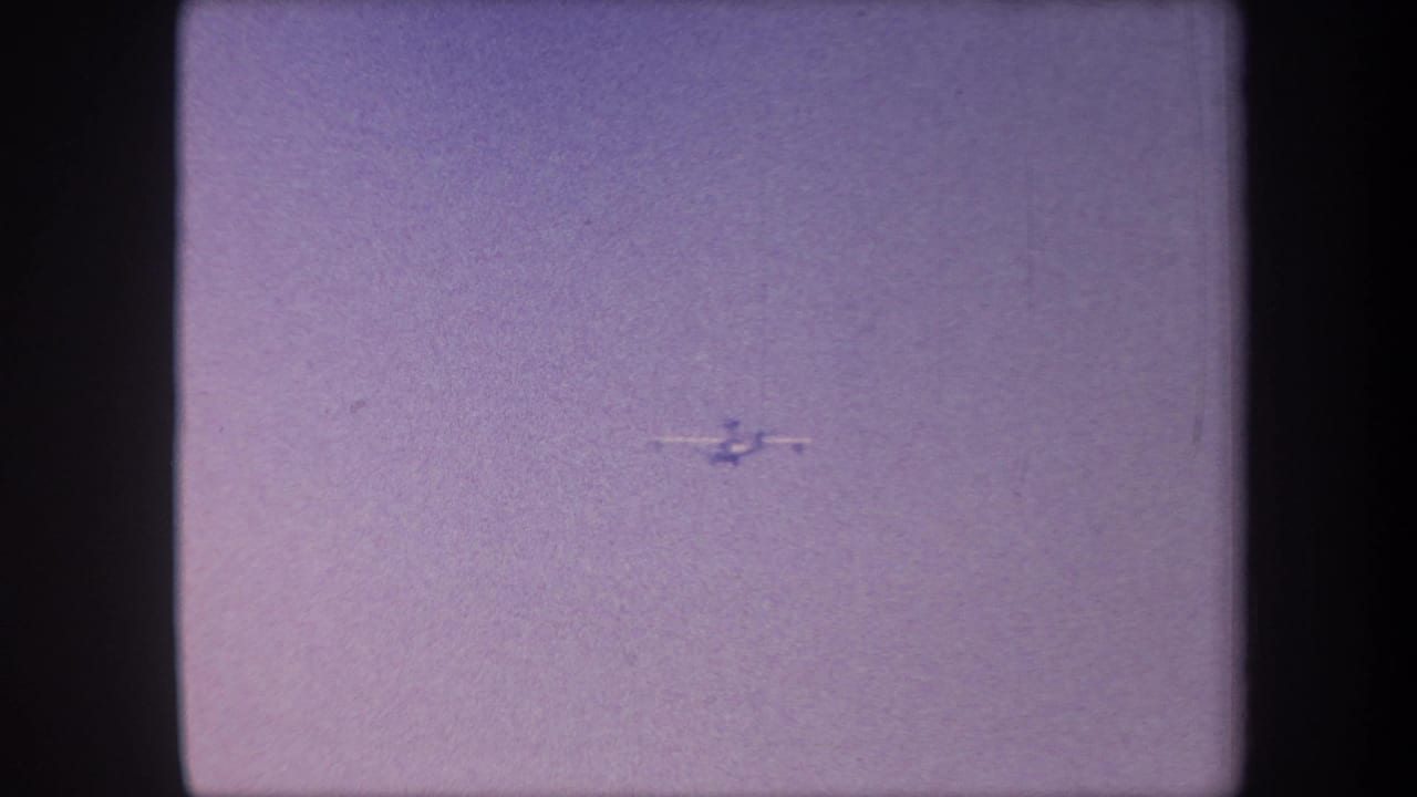 Small aircraft mid-flight against a hazy lavender sky in 8mm home movie footage attributed to Yucaipa, California, circa 1959.