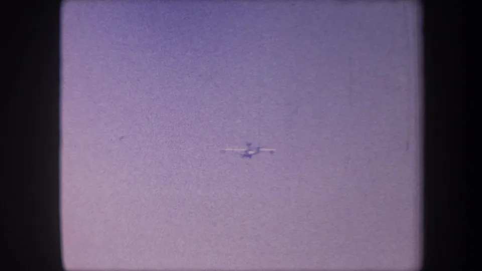 Small aircraft mid-flight against a hazy lavender sky in 8mm home movie footage attributed to Yucaipa, California, circa 1959.