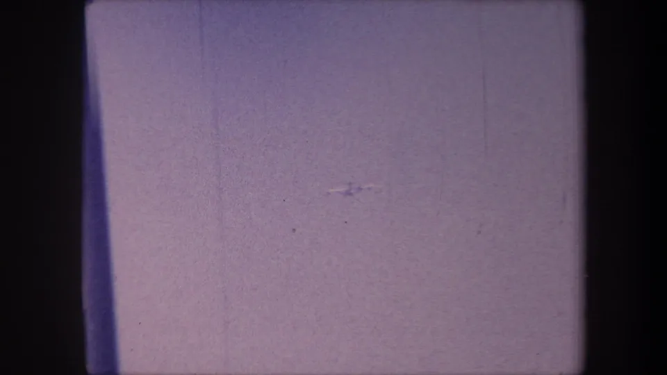 Opening frame of a 1959 8mm home movie; almost entirely consumed by a purple emulsion shift, with a possible faint aircraft speck visible at distance.
