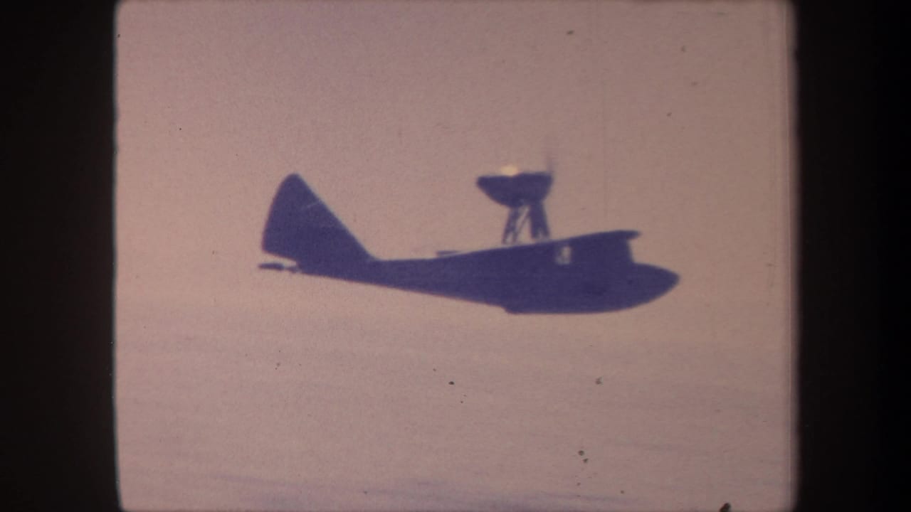 Seaplane in flight as a dark silhouette against a pale washed-out sky, from a 1959 California 8mm home movie