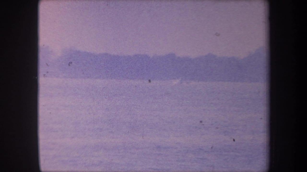 1959 8mm home movie frame showing calm water and a distant dark shoreline under a pale lavender sky, Yucaipa area, California.