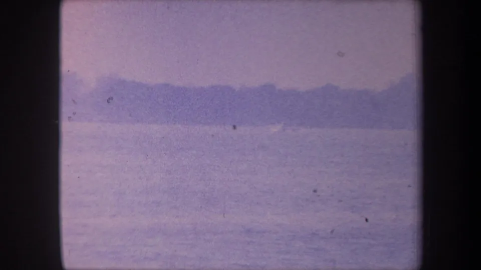 1959 8mm home movie frame showing calm water and a distant dark shoreline under a pale lavender sky, Yucaipa area, California.