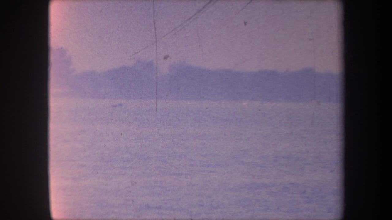 1959 California 8mm home movie — calm water, distant tree silhouettes at the horizon, blue-purple color cast with fine film scratches.