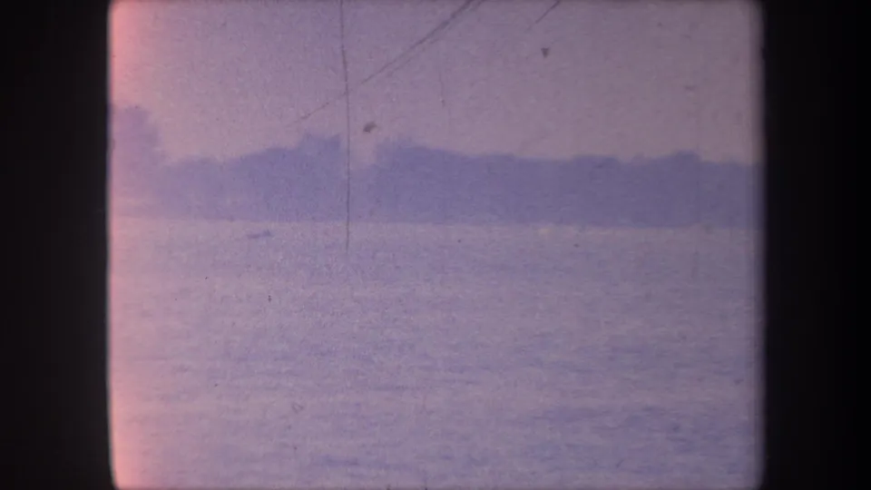 1959 California 8mm home movie — calm water, distant tree silhouettes at the horizon, blue-purple color cast with fine film scratches.