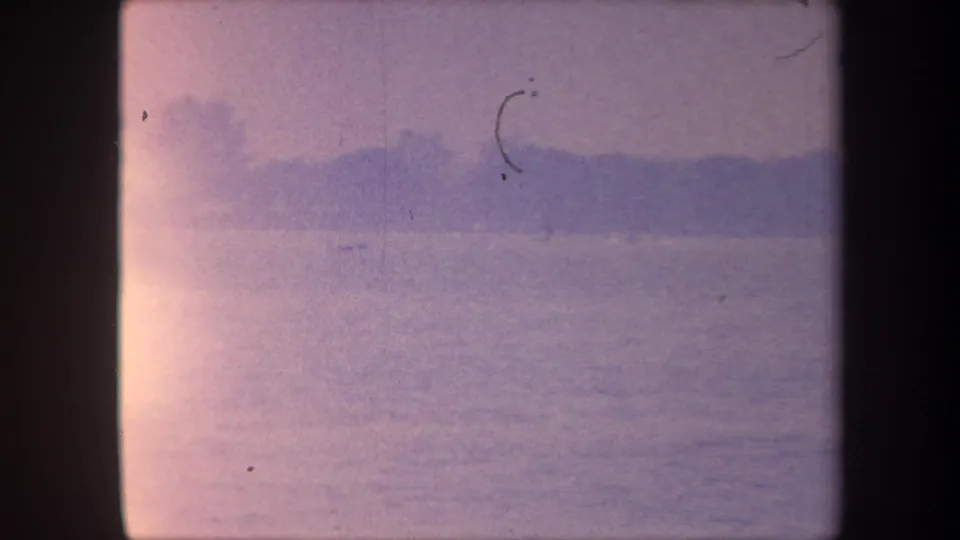 1959 California 8mm home movie — water surface, distant silhouetted shore, and a distinctive curved emulsion-scratch loop artifact mid-frame.