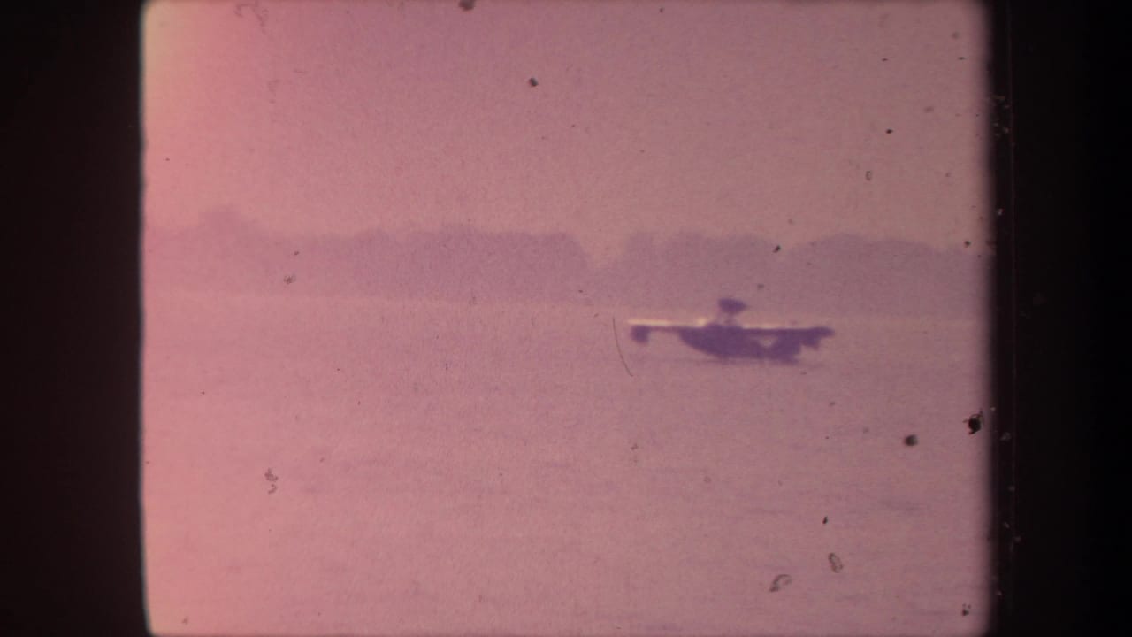 Seaplane silhouette on a pink-shifted lake surface with a faint distant treeline.