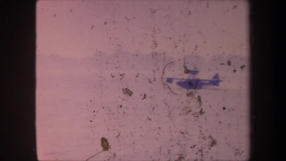 Heavily deteriorated 8mm frame circa 1959 showing seaplane on a California lake; a large emulsion damage patch and dense debris obscure much of the image.