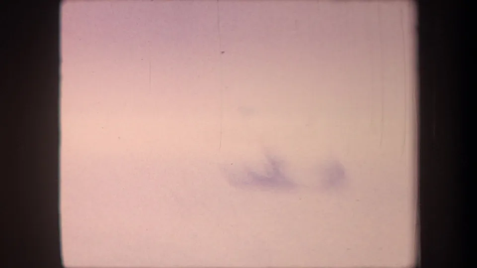 Heavily overexposed final frame of an 8mm home-movie reel, probable end-of-roll light leak with a faint indistinct shape barely visible