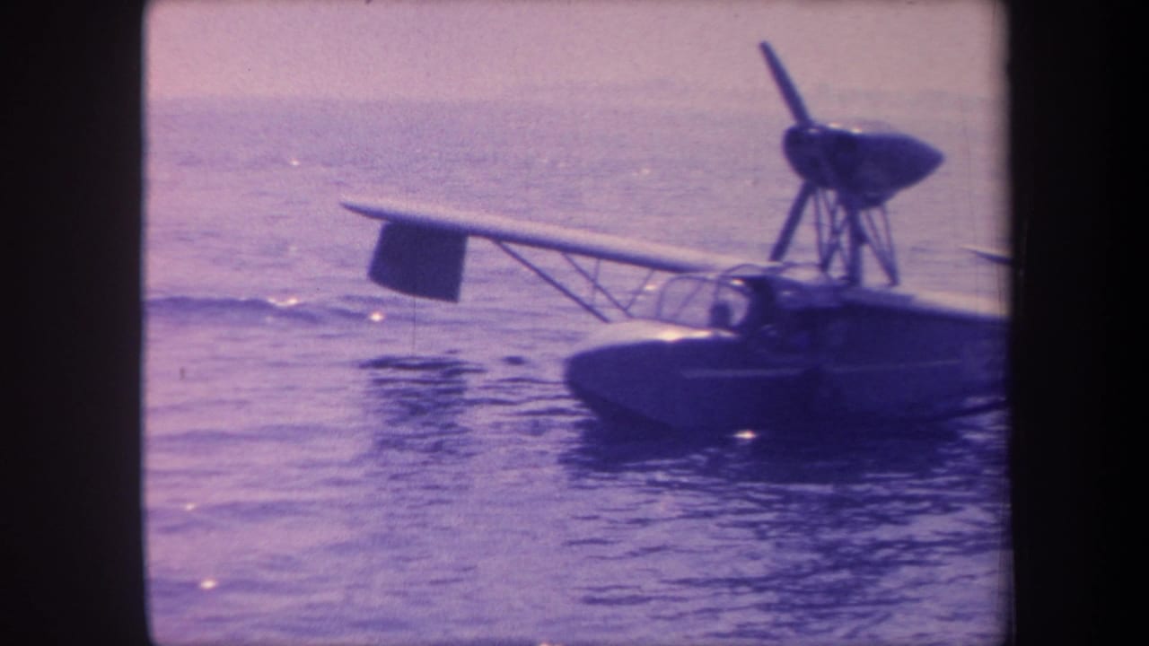 1959 8mm home-movie frame of a small flying-boat amphibian maneuvering on water, California; pronounced purple-blue film aging and visible grain.