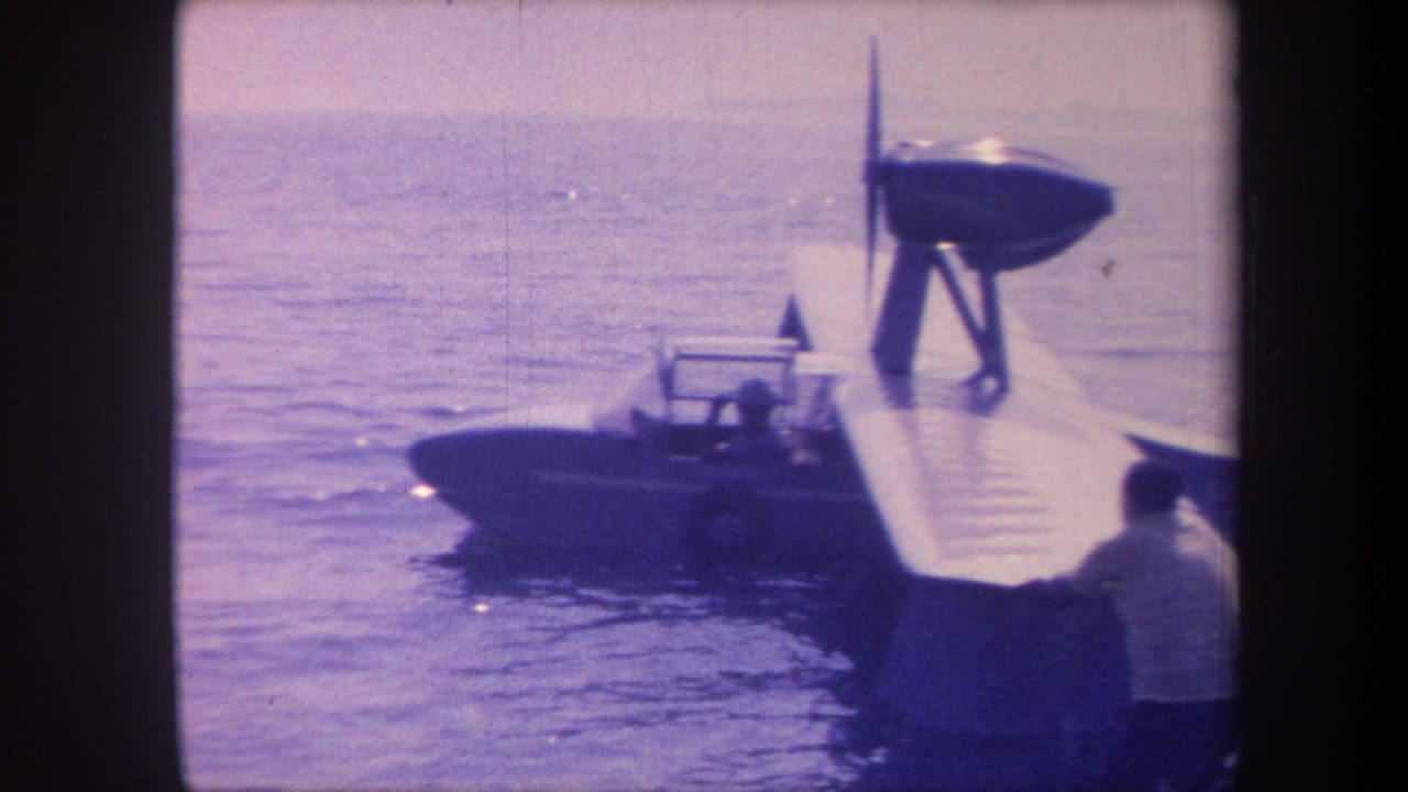 8mm home-movie frame, c. 1959, showing a single-engine flying boat floating on open water in California, with a person standing near the aircraft.