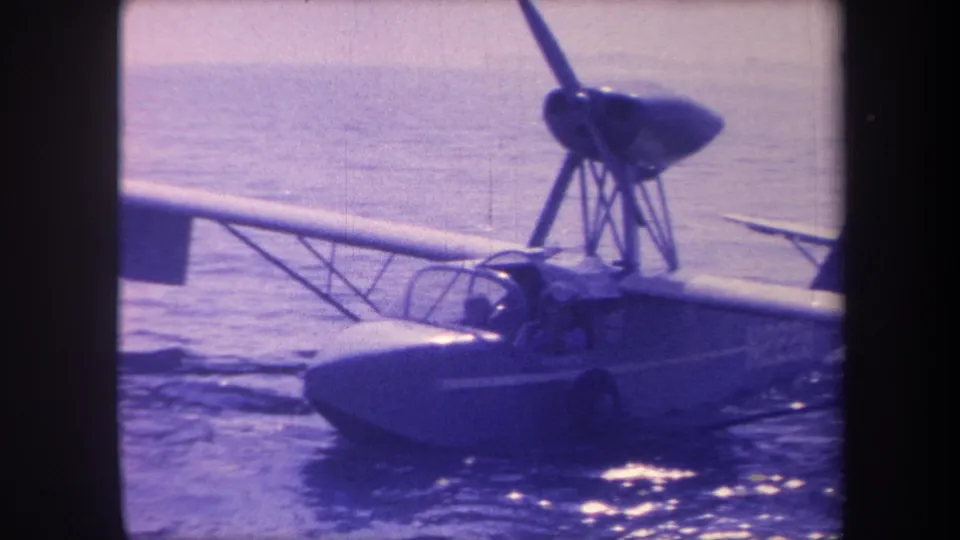 8mm home-movie frame circa 1959 showing the boat hull and pylon-mounted propeller of a small flying-boat seaplane on coastal water, Southern California.