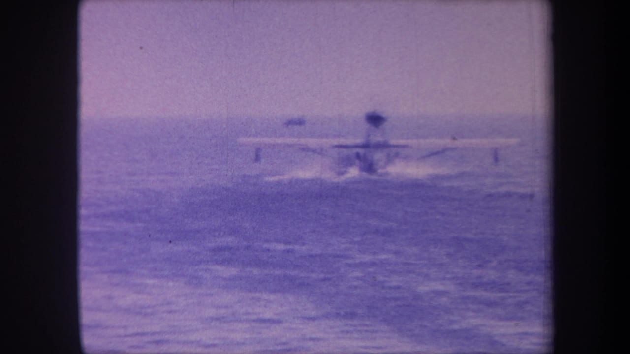 Small fixed-wing seaplane landing or taxiing on open ocean water, 1959 home movie, strong purple dye shift from aged 8mm stock.