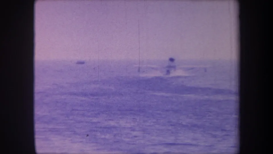 Seaplane silhouette on open ocean near sequence end, 1959 home movie, faded lavender tones from aged 8mm emulsion.