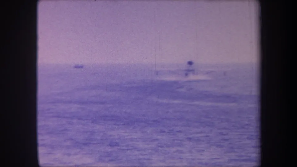 8mm home movie frame circa 1959 showing a distant motorboat on open sea, heavy magenta/violet dye-shift coloration and a faint second vessel on the far-left horizon.