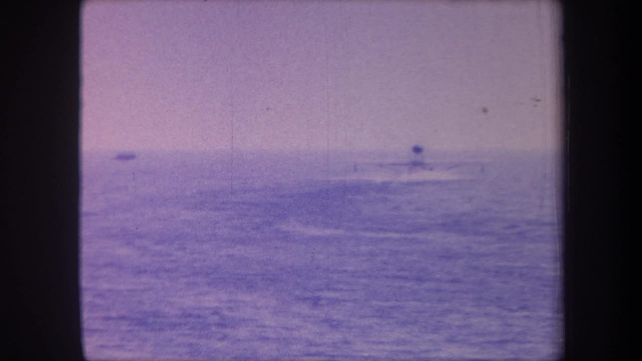 Open sea with strong purple color cast, small boat in the mid-distance, pale overcast sky.