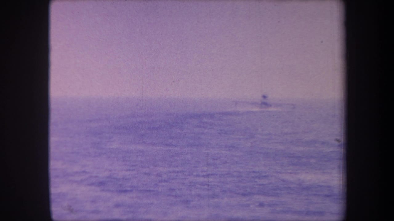 Blue-purple hued 8mm frame of open water with a small distant silhouette near the horizon.