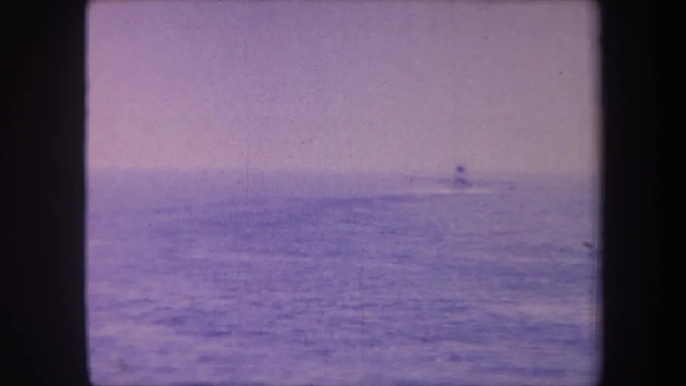 Open water under a pale sky, heavy blue-purple color cast from aged 8mm stock; small aircraft or watercraft silhouette at the horizon, circa 1959 California.