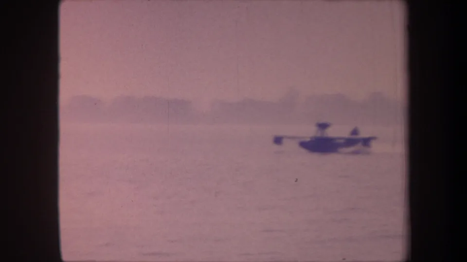 The floatplane appears larger in frame as it moves across the lake in this 1959 8mm home-movie footage; strong magenta dye-shift throughout.