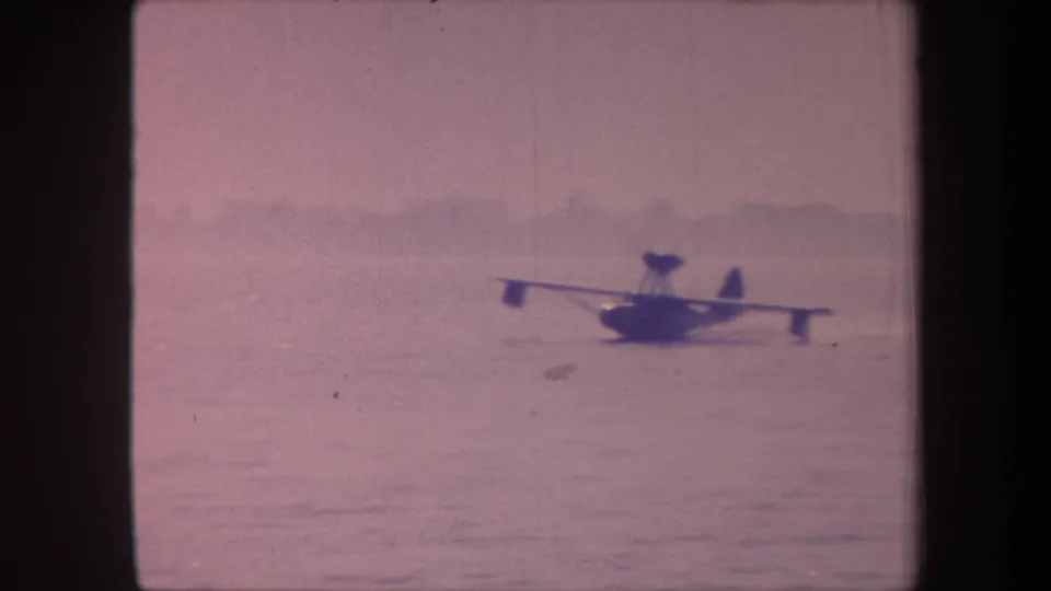 Floatplane continues across the lake; distant hills on horizon in this aged 1959 8mm home-movie frame with strong pink-magenta dye-shift.